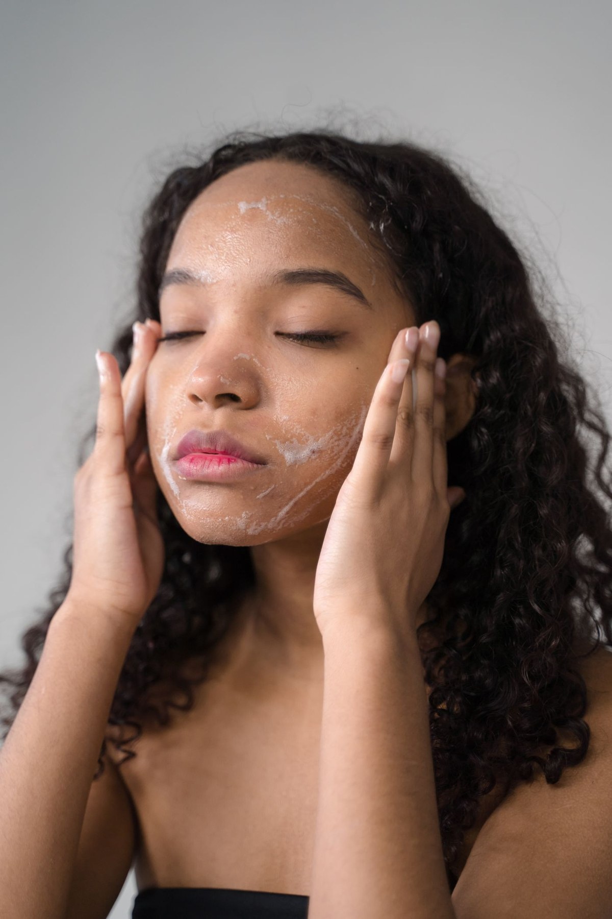 A woman applies facial wash to her face