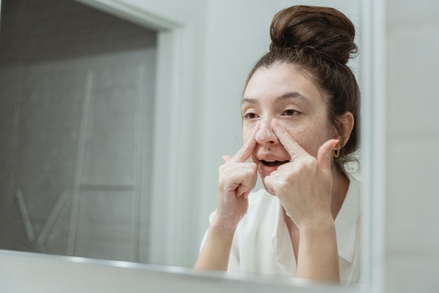 A woman washes her face at a bathroom mirror