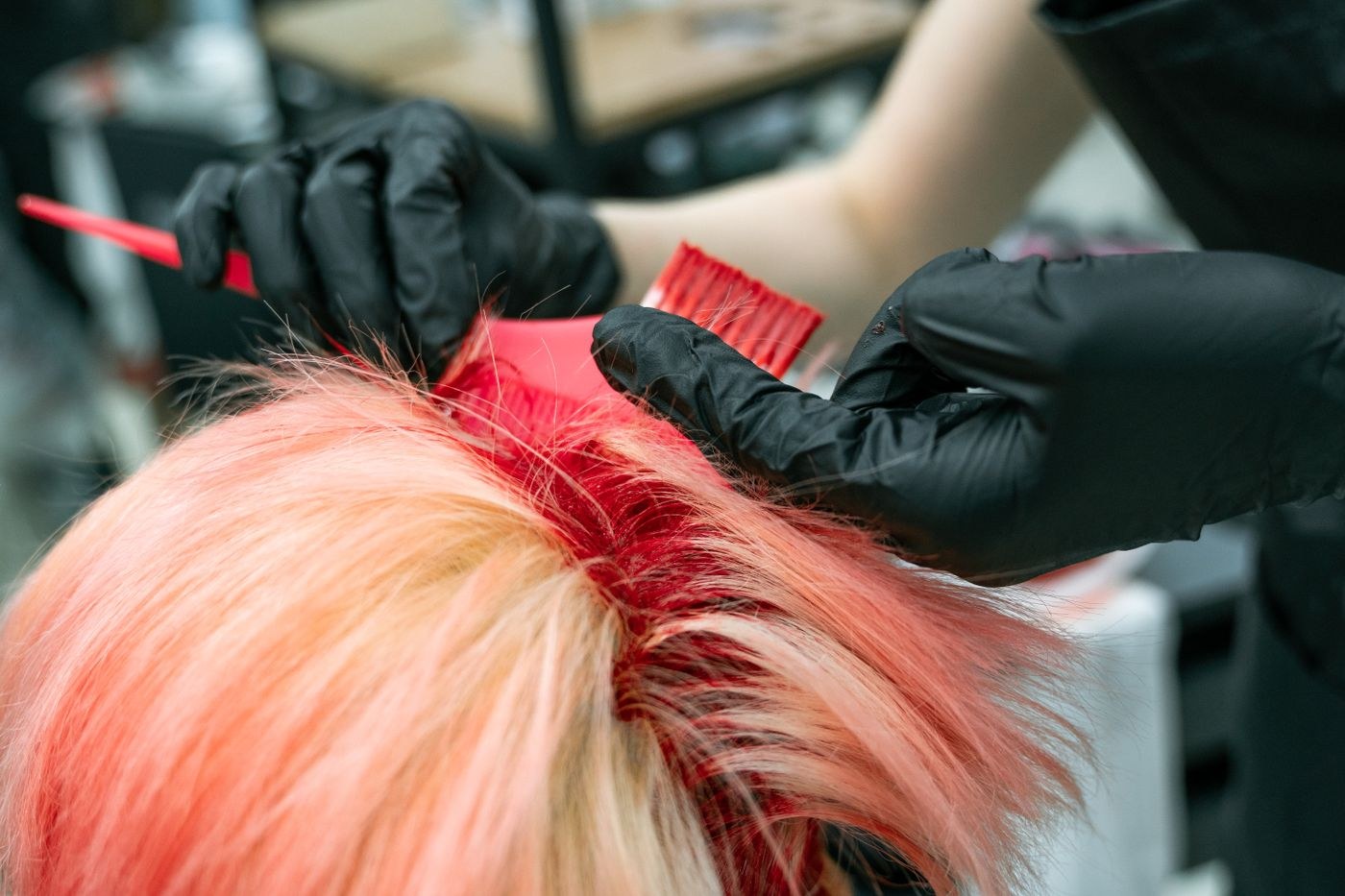 Gloved hands apply hair dye to a section of hair