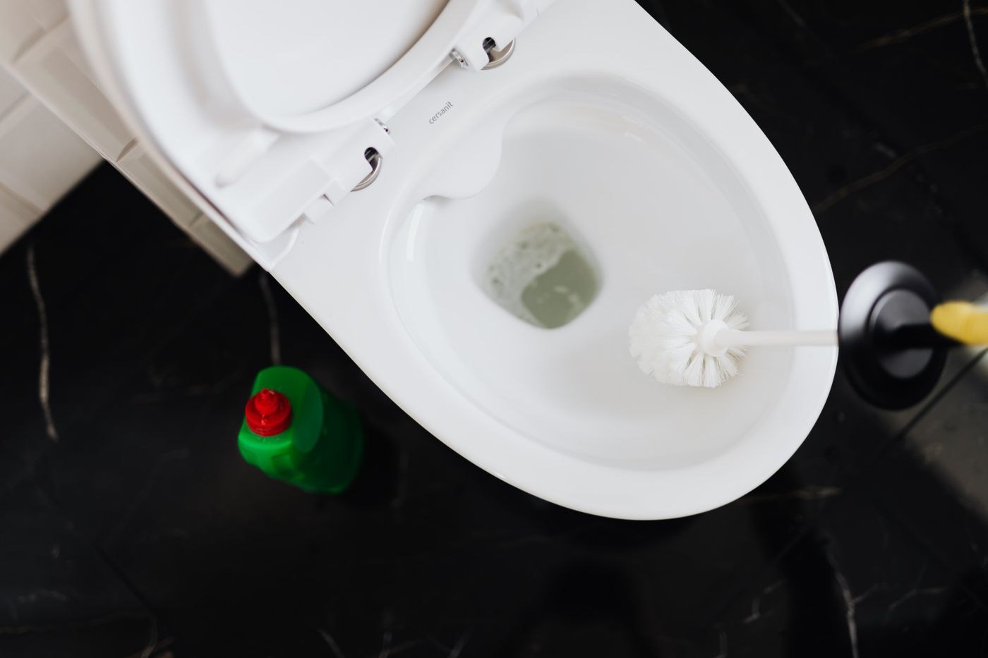 Gloved hands clean a toilet bowl using a toilet brush