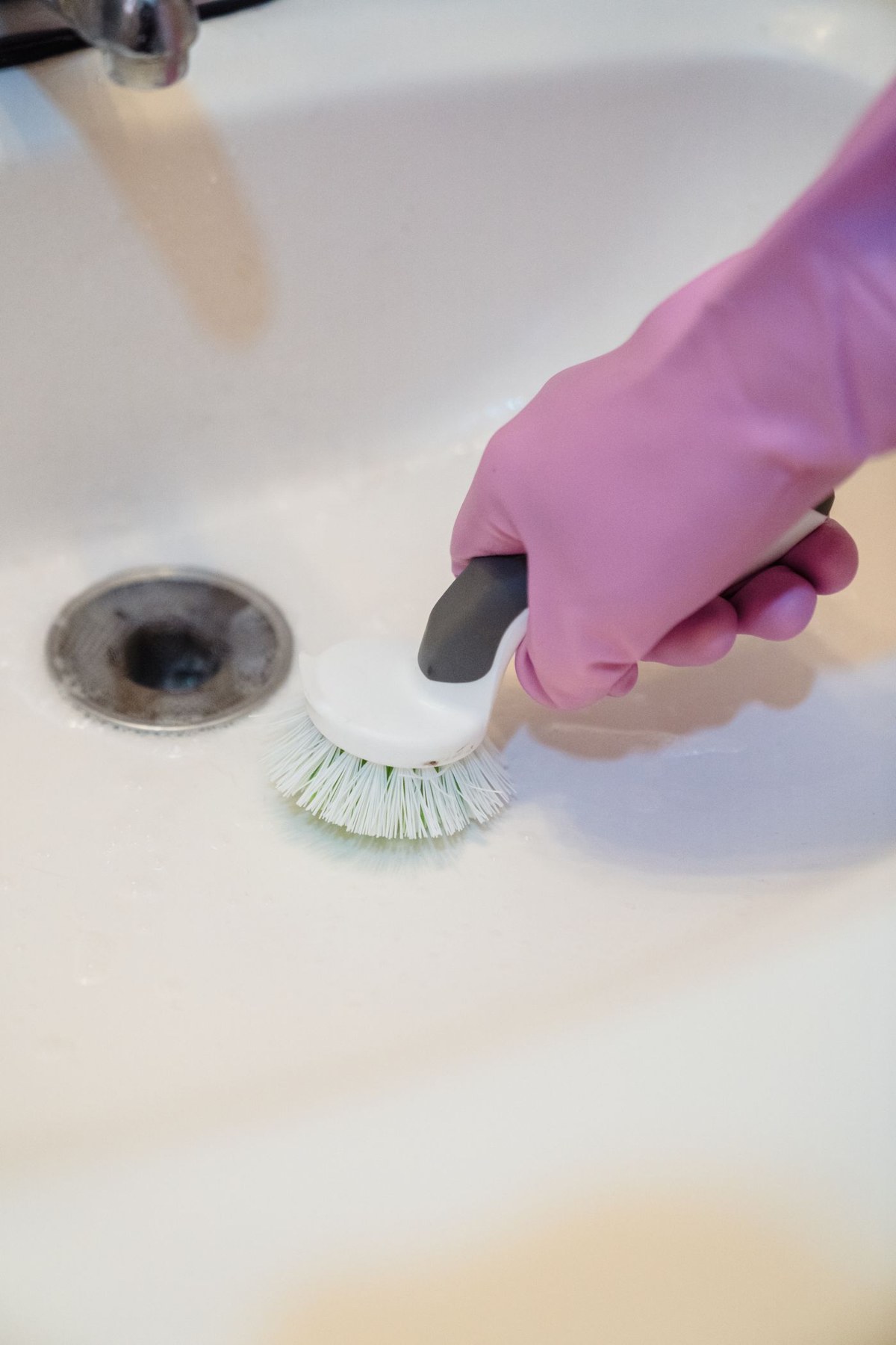 A gloved hand uses a scrub brush on a sink
