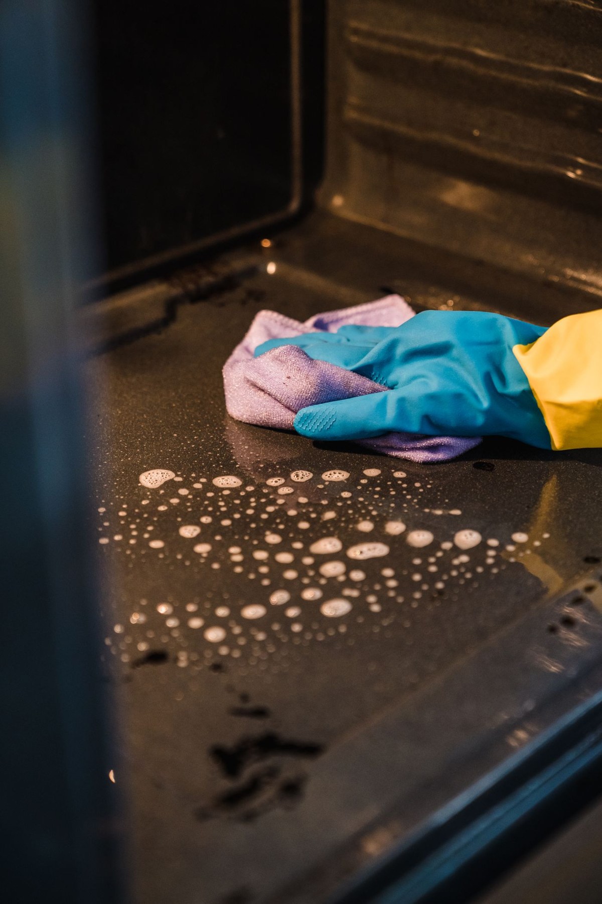 A gloved hand wipes the inside of an oven