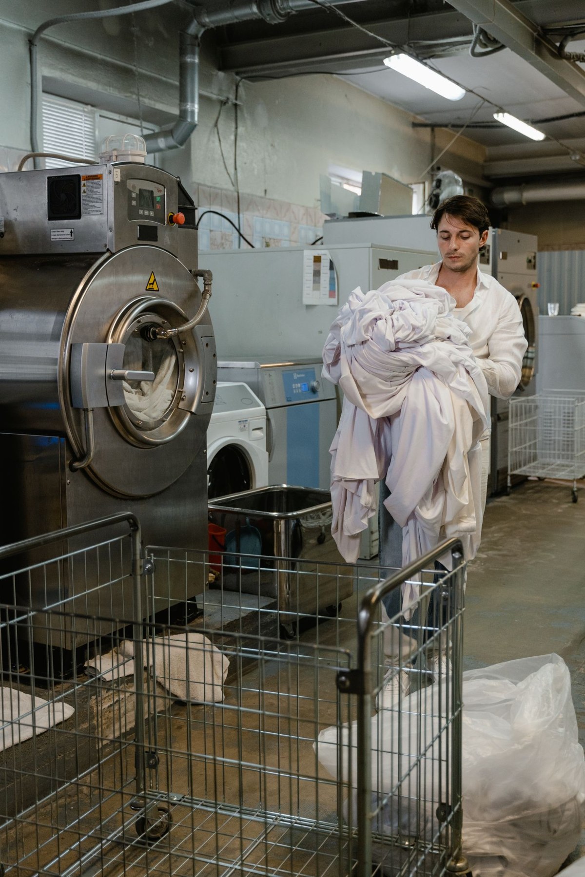 A person carries bed linen beside laundry machines